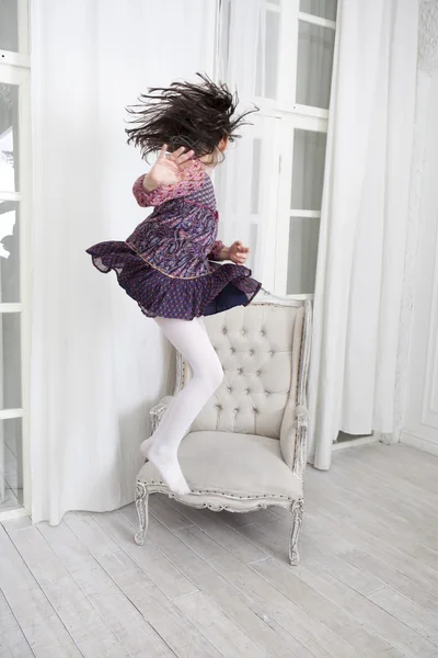 Little girl in dress  jumping from chair. — Stock Photo, Image