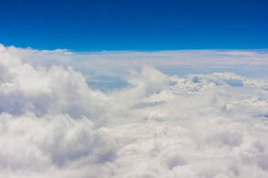 Kabarık beyaz bulutlar ve mavi gökyüzü uçaktan görünüyor..