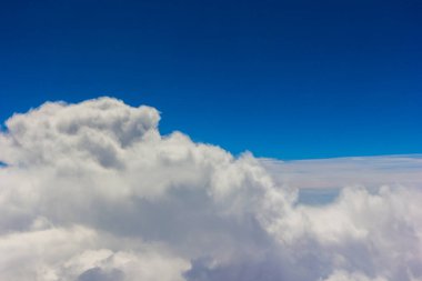 Kabarık beyaz bulutlar ve mavi gökyüzü uçaktan görünüyor..