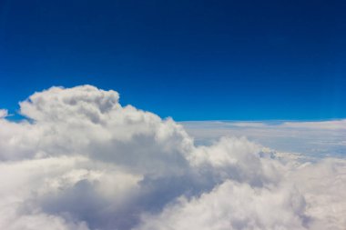 Kabarık beyaz bulutlar ve mavi gökyüzü uçaktan görünüyor..