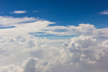 Kabarık beyaz bulutlar ve mavi gökyüzü uçaktan görünüyor..