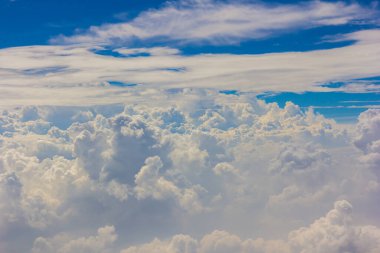 Kabarık beyaz bulutlar ve mavi gökyüzü uçaktan görünüyor..