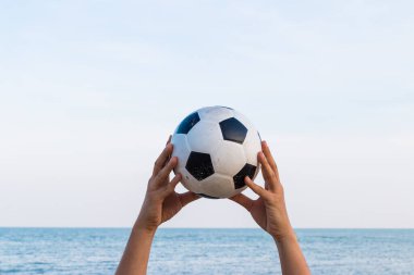 Arka planda deniz olan bir futbol topunu tutan bir adam.