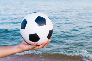 Arka planda deniz olan bir futbol topunu tutan bir adam.
