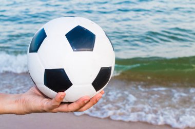 Arka planda deniz olan bir futbol topunu tutan bir adam.