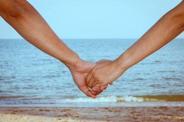 Gökyüzü, sahil ve kumla el ele tutuşan çiftlere yakın durun.