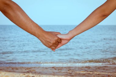 Gökyüzü, sahil ve kumla el ele tutuşan çiftlere yakın durun.