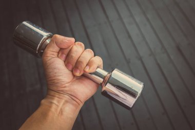 Klasik stil. El, siyah ahşap arka planda çelik dambıl tutuyor.