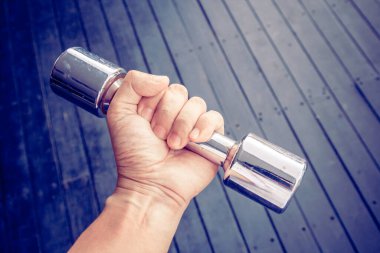 Klasik stil. El, siyah ahşap arka planda çelik dambıl tutuyor.