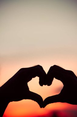 Aşk işareti. Gün batımında el silueti kalp sembolü. Eski tarz arkaplan