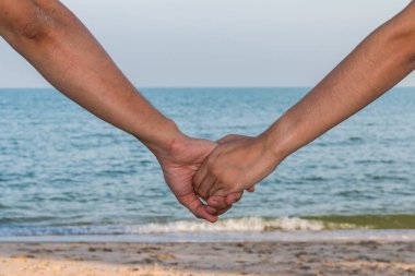 Gökyüzü, sahil ve kumla el ele tutuşan çiftlere yakın durun.