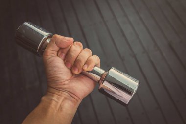 Klasik stil. El, siyah ahşap arka planda çelik dambıl tutuyor.