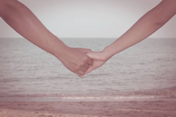 Close up of couple holding hands with sky, beach and sand background