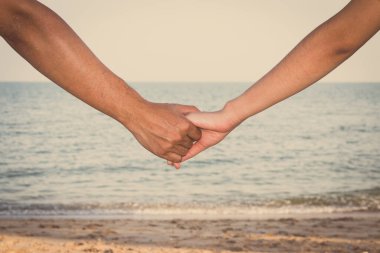 Gökyüzü, sahil ve kumla el ele tutuşan çiftlere yakın durun.