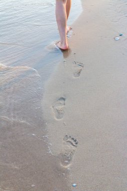 Yalnız kız dalgalı ayak izleriyle kumda yürüyor.