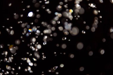 Su damlaları havada süzülüyor. Işıkla yansıtılıyor.