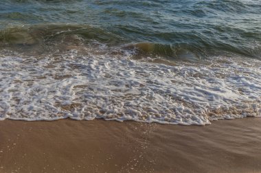 Güneşli bir günde kumlu sahilde denizin dalgası