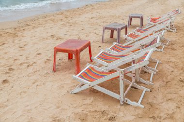 Beyaz ahşap plaj sandalyesi ve kumsaldaki eski kırmızı plaj masası.