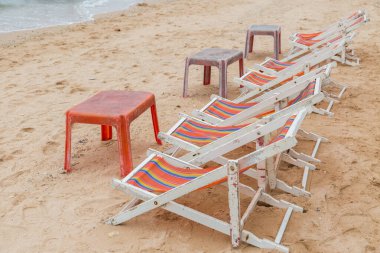 Beyaz ahşap plaj sandalyesi ve kumsaldaki eski kırmızı plaj masası.