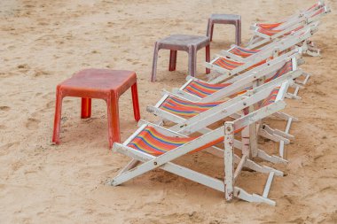 Beyaz ahşap plaj sandalyesi ve kumsaldaki eski kırmızı plaj masası.