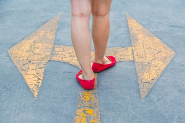 Kırmızı ayakkabılı bir kız asfalt bir arka planda sarı trafik okuna doğru yürüyor.