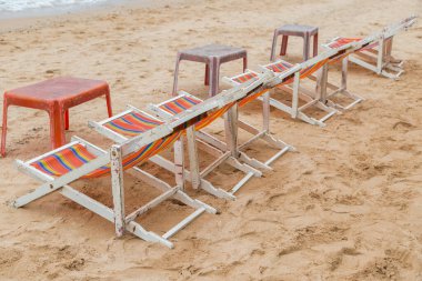 Beyaz ahşap plaj sandalyesi ve kumsaldaki eski kırmızı plaj masası.