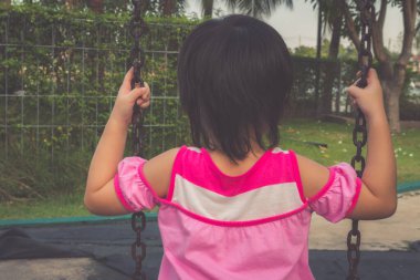 Küçük kız parkta salıncak oynarken eğleniyor.