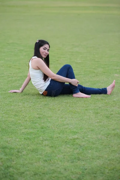 緑の草の背景に青いジーンズを着た緑の草の上に横たわるリラックスした女性 — ストック写真