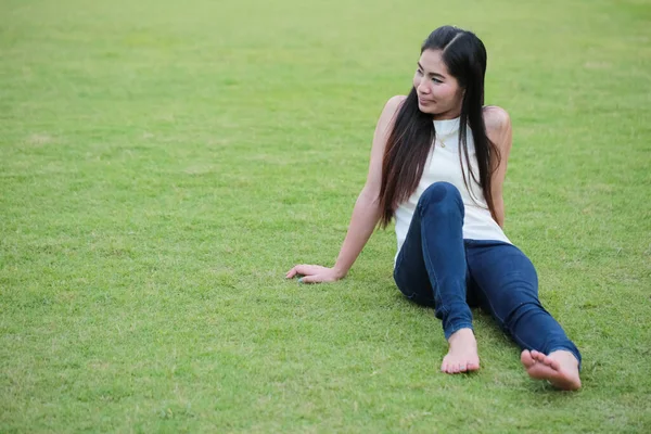 緑の草の背景に青いジーンズを着た緑の草の上に横たわるリラックスした女性 — ストック写真