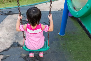 Küçük kız parkta salıncak oynarken eğleniyor.