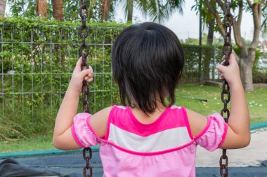 Küçük kız parkta salıncak oynarken eğleniyor.