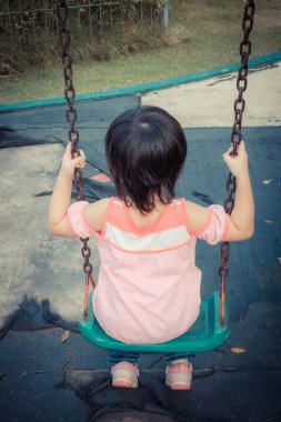 Küçük kız parkta salıncak oynarken eğleniyor.