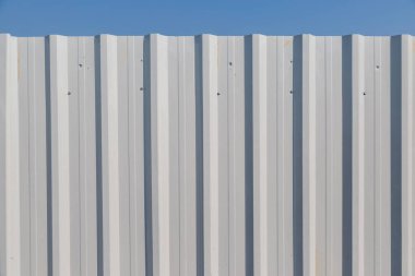 Mavi gökyüzü arkaplanlı beyaz eğimli metal tel örgü.