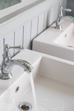 Beyaz lavabo arka planına sahip açık bir musluktan akan su.