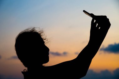 Gün batımında selfie çeken bir kadının siluet fotoğrafı.