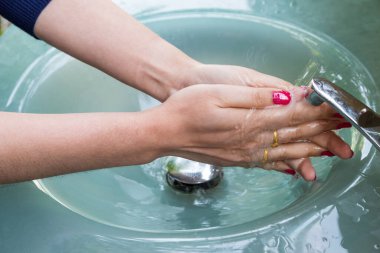 Kırmızı tırnaklı, elleri temizleyen, ellerini mavi lavaboda yıkayan kadın.