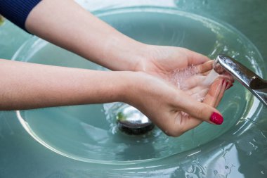 Kırmızı tırnaklı, elleri temizleyen, ellerini mavi lavaboda yıkayan kadın.