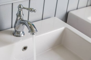 Beyaz lavabo arka planına sahip açık bir musluktan akan su.