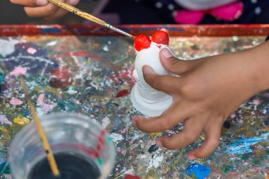 Bir çocuk masanın üzerine beyaz alçı bebek oyuncakları boyuyor.