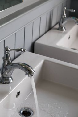 Beyaz lavabo arka planına sahip açık bir musluktan akan su.