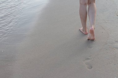 Kumsalda tek başına yürüyen bir kadın kumların arkasında ayak izleri bırakıyor.