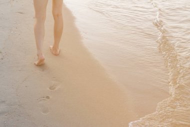 Kumsalda tek başına yürüyen bir kadın kumların arkasında ayak izleri bırakıyor.