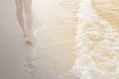 Kumsalda tek başına yürüyen bir kadın kumların arkasında ayak izleri bırakıyor.