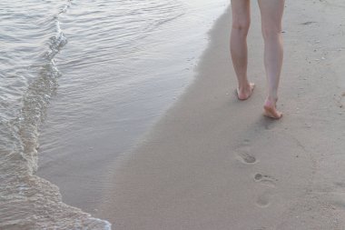 Kumsalda tek başına yürüyen bir kadın kumların arkasında ayak izleri bırakıyor.