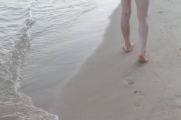 Kumsalda tek başına yürüyen bir kadın kumların arkasında ayak izleri bırakıyor.