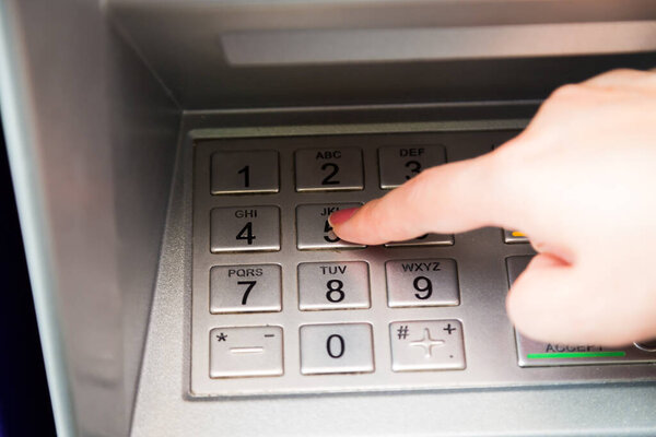 Close up of hand entering pin code at ATM machine to withdraw her money