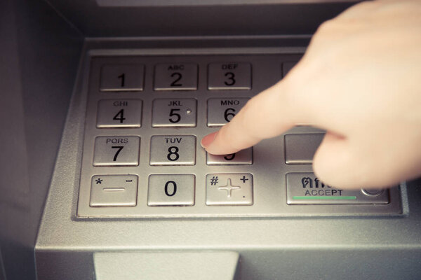 Close up of hand entering pin code at ATM machine to withdraw her money