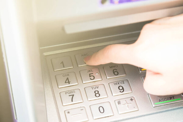 Close up of hand entering pin code at ATM machine to withdraw her money