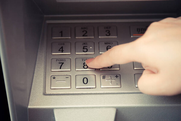 Close up of hand entering pin code at ATM machine to withdraw her money