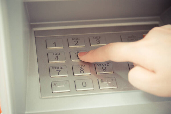 Close up of hand entering pin code at ATM machine to withdraw her money